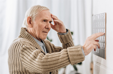 [Translate to Deutsch:] Old man touching his forehead standing infront of an button panel